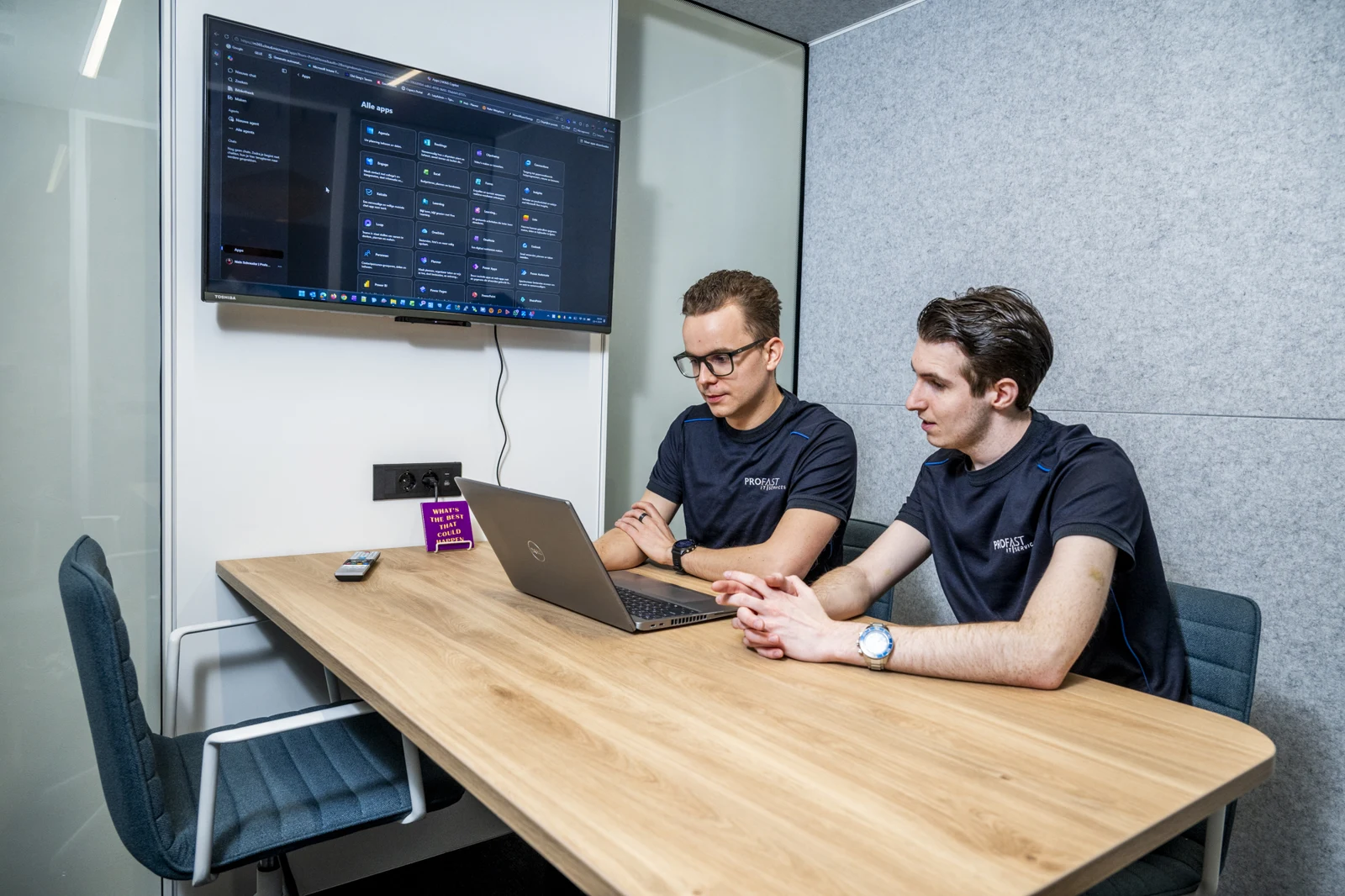 Twee Profast-medewerkers overleggen bij een laptop en een scherm met Microsoft 365